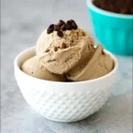 Dairy free coffee ice cream scoop topped with caramel and cocoa nibs in a ceramic bowl